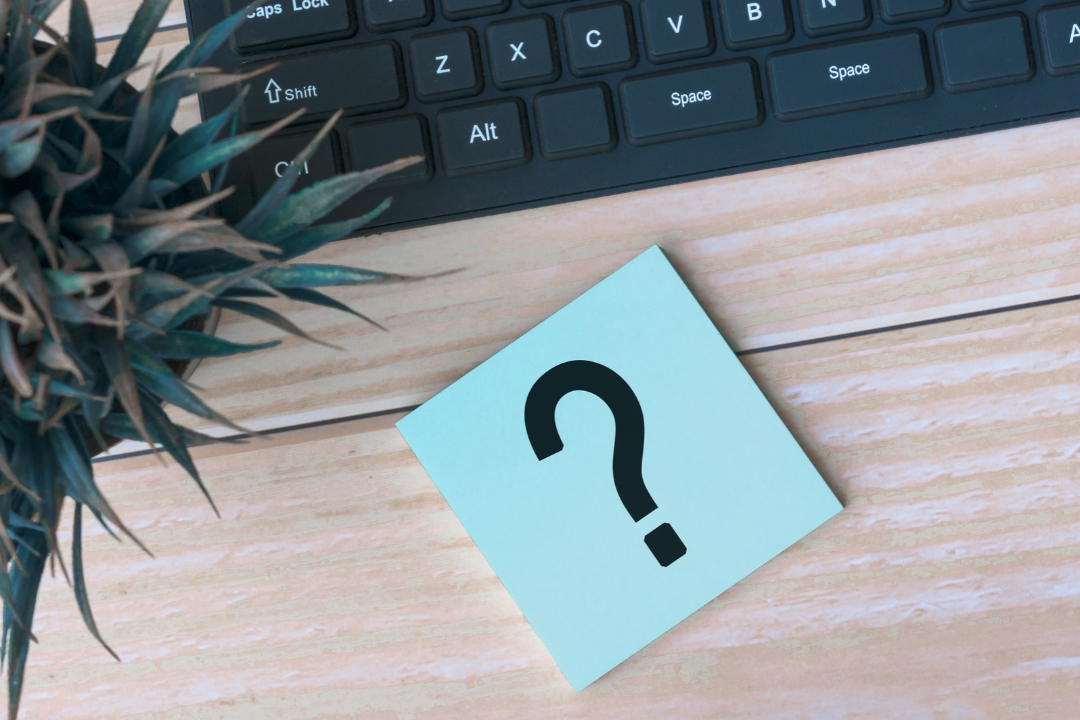 Post it with a question mark on a desk with a keyboard